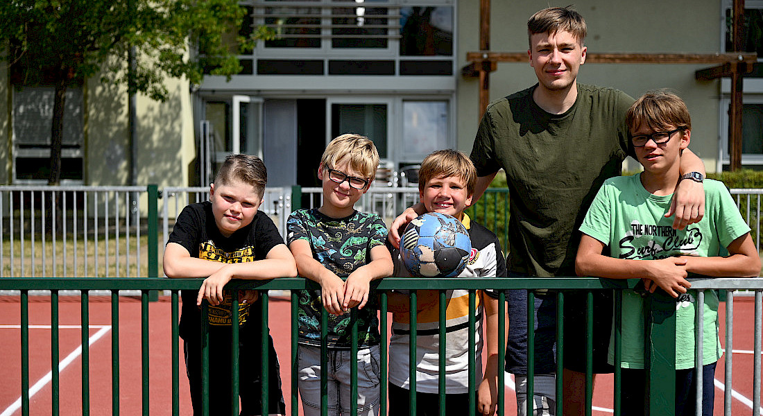 Vier Kinder und ein Erwachsener stehen auf einem Sportplatz mit Basketball.