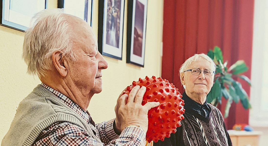 Zwei Personen werfen sich einen roten Ball mit Noppen zu.