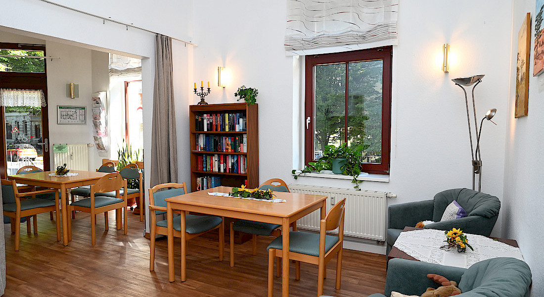 Heller Aufenthaltsraum mit Tischen, Stühlen und einem Sofa in wohnlicher Gestaltung.