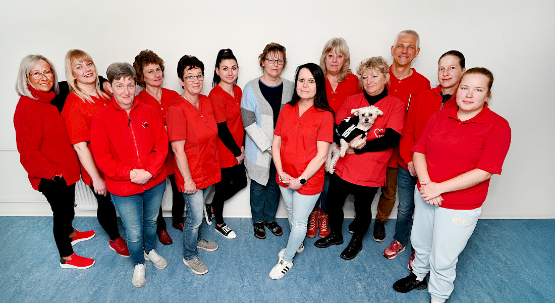 Teamfoto mit 13 Personen, die meisten tragen ein rotes Shirt.