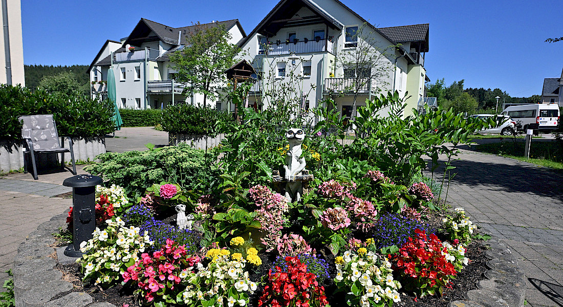 Rundbeet mit bunten Blumen im Innenhof vor einem Wohngebäude.