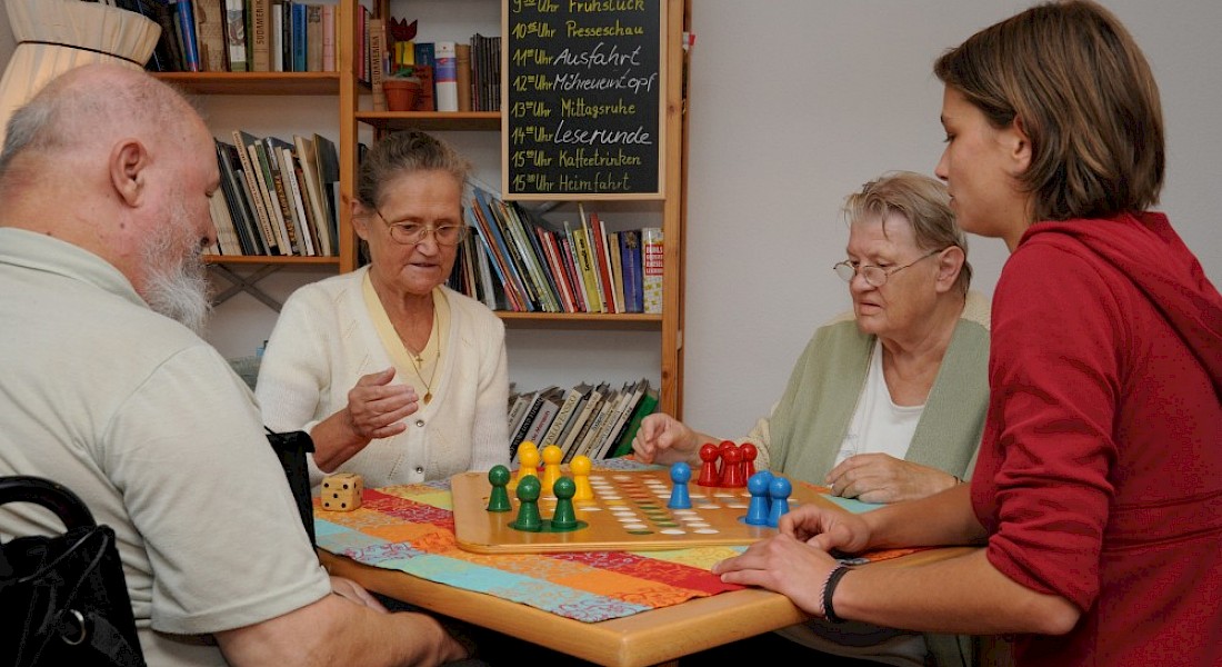 Vier Personen sitzen am Tisch, spielen ein Brettspiel.