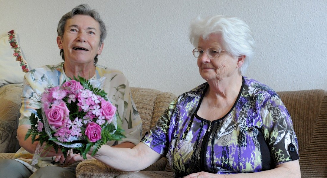 Zwei Personen halten einen bunten Blumenstrauß und lächeln.