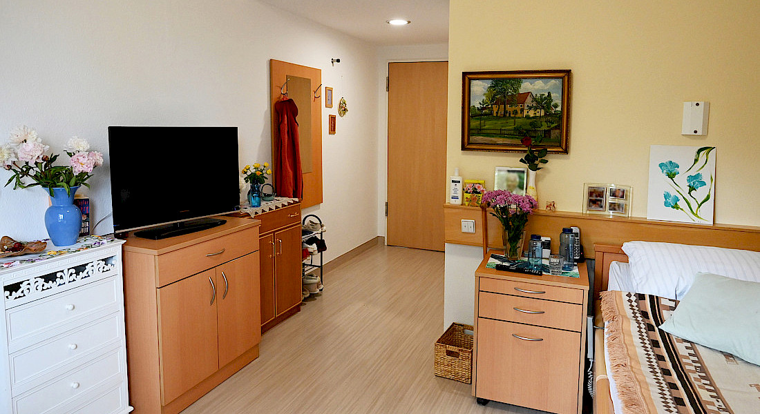 Ein gemütlich eingerichtetes Einzelzimmer mit Fernseher, Bildern und Möbeln.