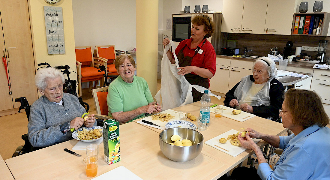 Vier ältere Personen sitzen um einen Tisch und bereiten gemeinsam mit einer Pflegekraft die Zutaten für das Kochen vor.