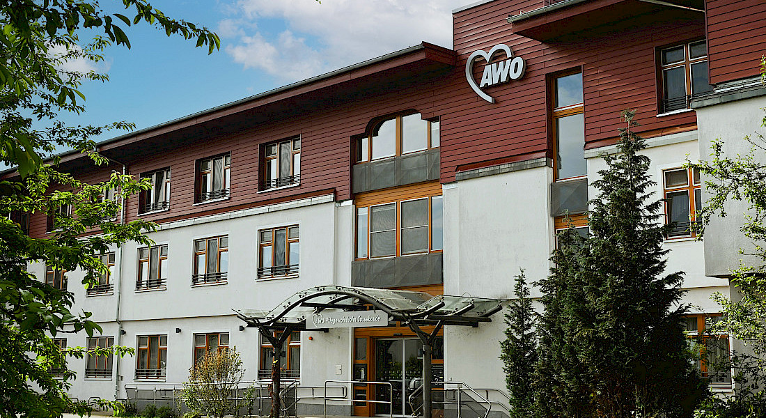 Außenansicht eines mehrstöckigen AWO-Gebäudes mit roter Holzfassade im obersten Stock.