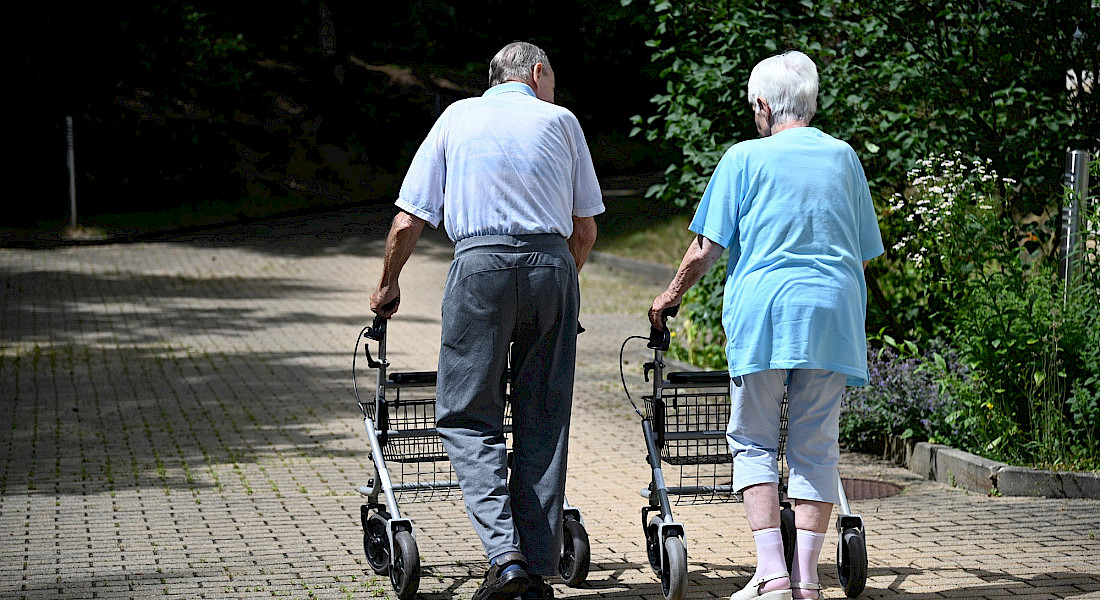 Zwei Personen gehen nebeneinander mit Rollatoren einen Weg entlang.