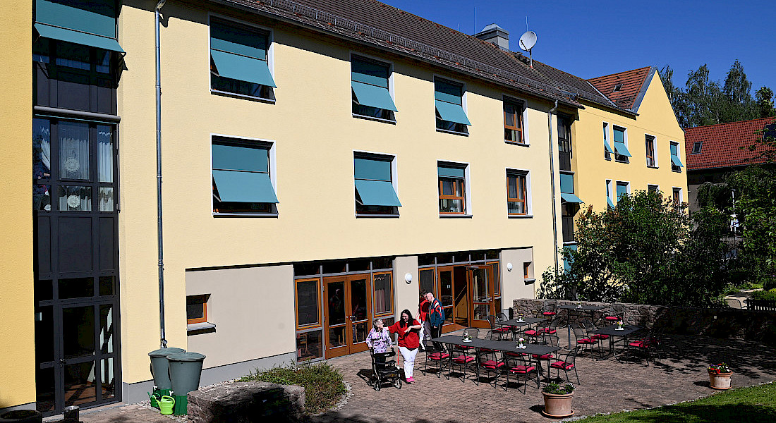 Außenansicht eines Wohnbereichs mit gelber Fassade, davor mit Personen.