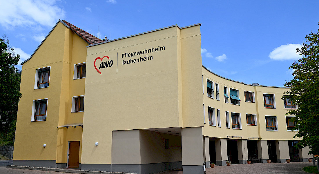 Außenansicht der Einrichtung mit gelber Fassade und großem AWO-Logo.
