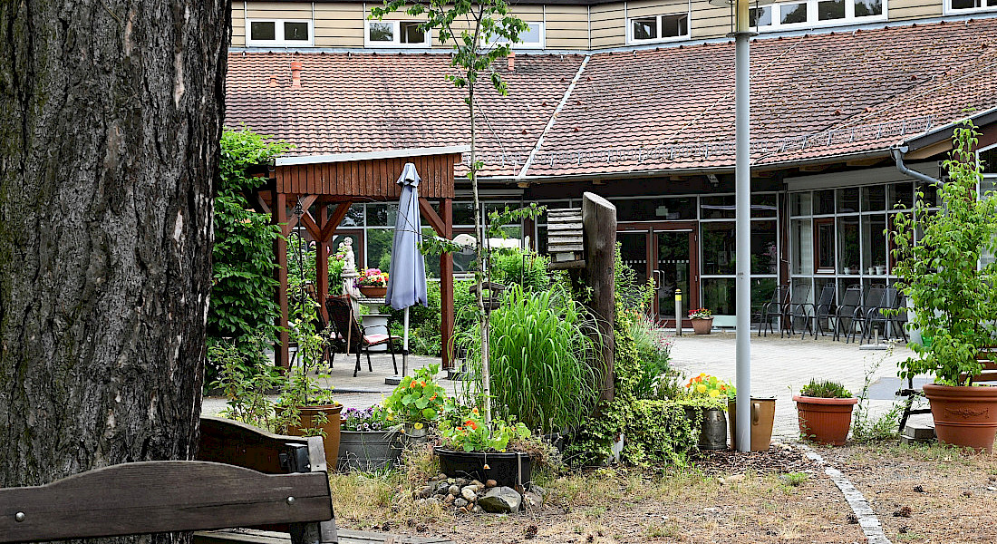 Gartenanlage mit Hochbeeten und Topfpflanzen vor einem Gebäude mit roten Dachziegeln.