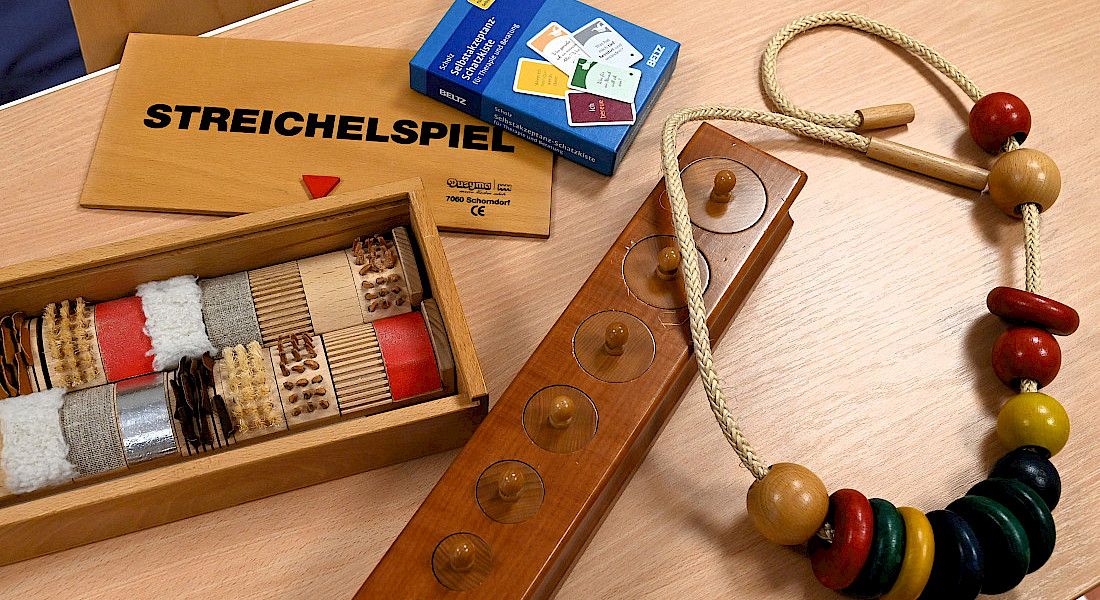 Verschiedene haptische Übungselemente und ein „Streichelspiel“-Set liegen auf einem Tisch.