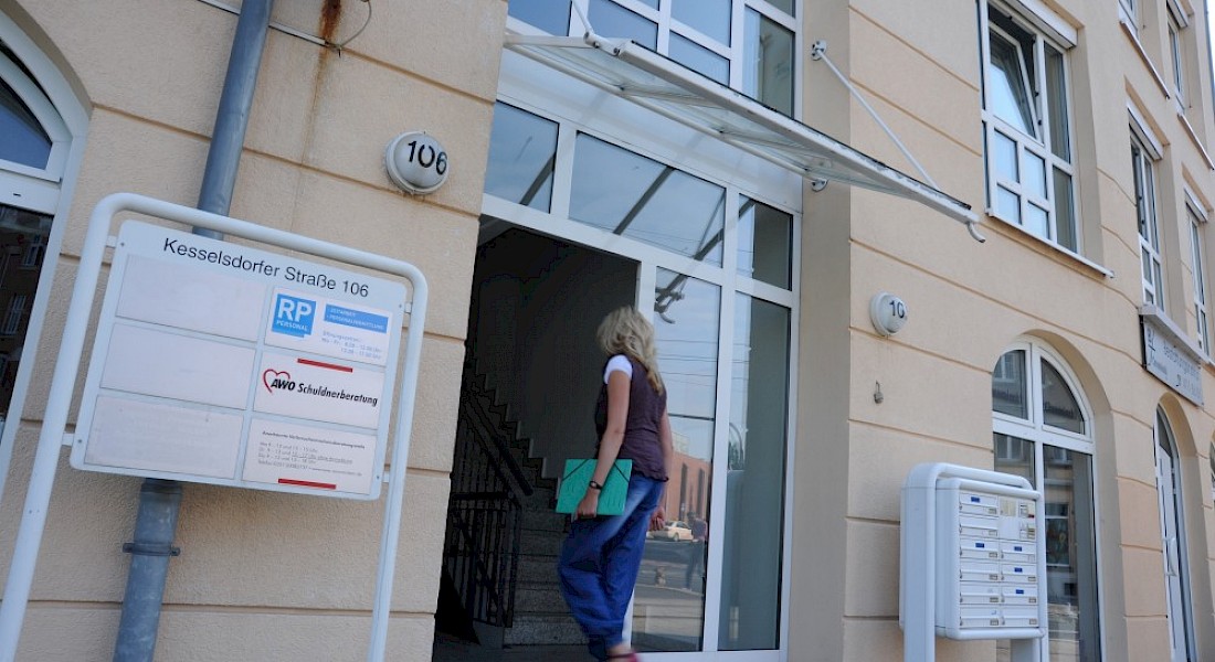 Eine Person betritt ein Gebäude mit heller Fassade und Glasdach über dem Eingang.