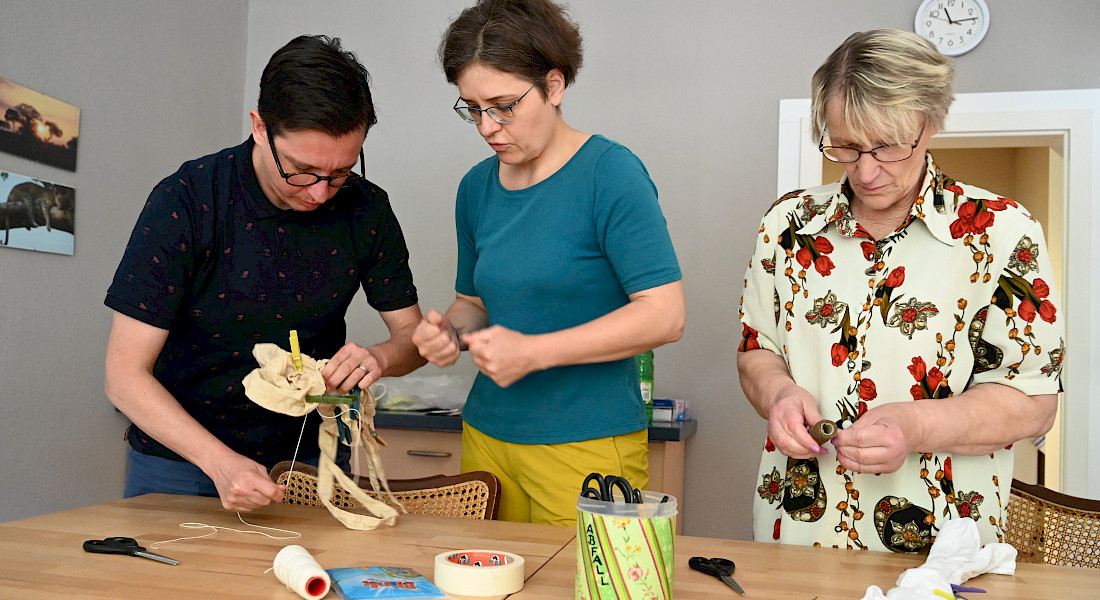 Drei Frauen basteln mit verschiedenen Materialien an einem Tisch.